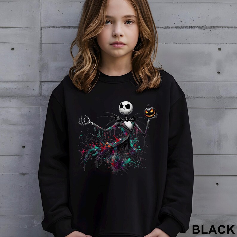 A young girl wearing a black sweatshirt with a graphic of a jack-o-lantern character on it.