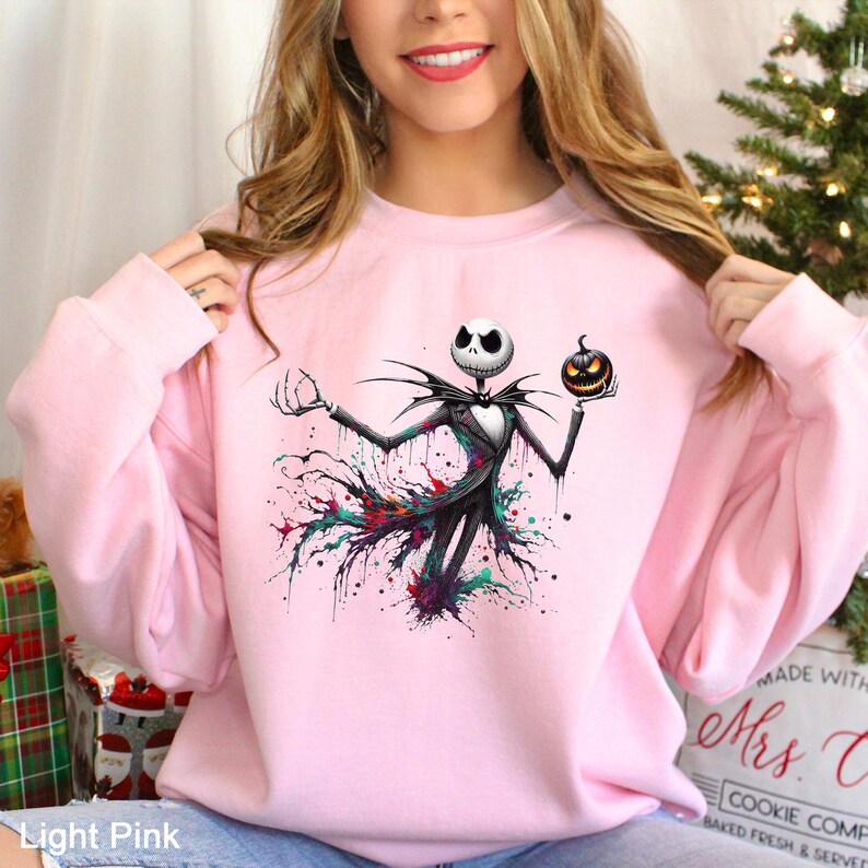 A woman wearing a pink sweatshirt with a graphic of a jack-o-lantern character from the movie " jack-o-lantern".