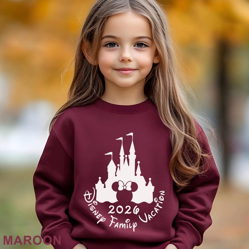 A young girl with long blonde hair wearing a maroon sweater with a white Disney castle and text printed on it.