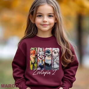 A young girl wearing a maroon sweater with a graphic of the Zootopia movie characters.