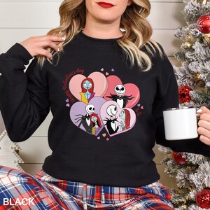 A woman wearing a black sweater with a graphic of characters from the movie " Nightmare Before Christmas" and holding a coffee mug.