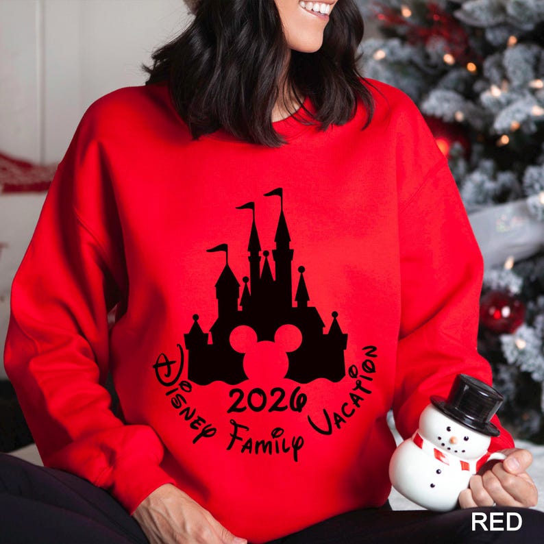 A woman wearing a red sweater with a black silhouette of a castle and the text "Disney Family Vacation 2020" printed on it, holding a small snowman toy.