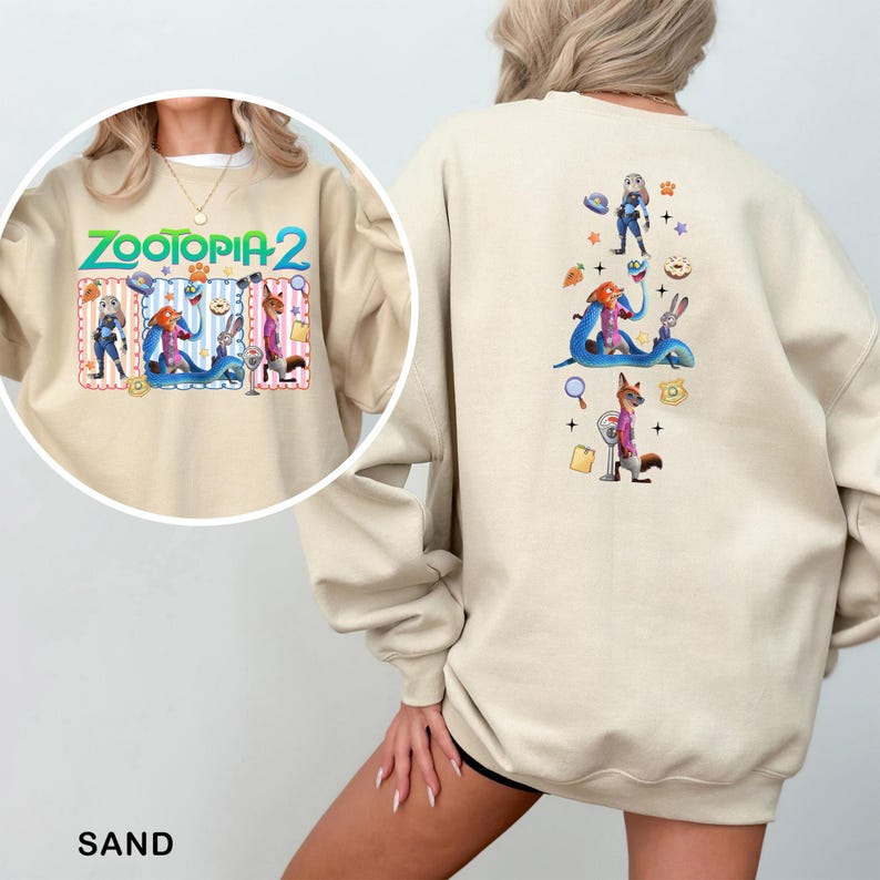 A person wearing a beige sweatshirt with a colorful graphic design featuring cartoon characters and various objects.