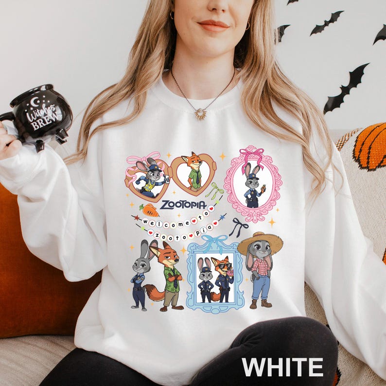 A woman wearing a white sweatshirt with a graphic of cartoon animals, including a fox, rabbit, and other animals, along with a mug and a necklace.