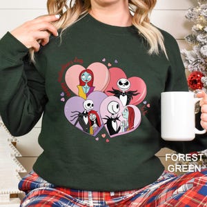 A woman wearing a green sweatshirt with a graphic design featuring characters from the movie " jack Skellington and Sally".