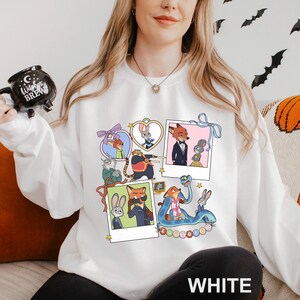 A woman wearing a white sweatshirt with a collage of cartoon animal characters on it, including a fox, rabbit, and other animals. She is holding a mug with a black design and is sitting on a couch.