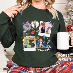 A woman wearing a green sweater with a collage of cartoon animal characters on it, holding a white mug.