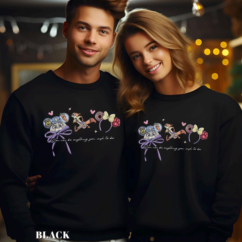 A man and a woman are standing next to each other, both wearing black sweatshirts with a whimsical design featuring a character and text.