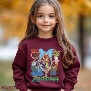 A young girl with long blonde hair is wearing a maroon sweater with a colorful graphic of cartoon characters from the movie "Zootopia".