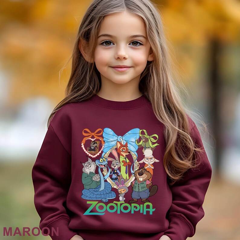 A young girl with long blonde hair is wearing a maroon sweater with a colorful graphic of cartoon characters from the movie "Zootopia".