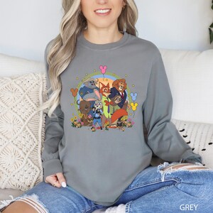 A woman wearing a grey long-sleeved shirt with a colorful graphic of cartoon animals and a group of people.