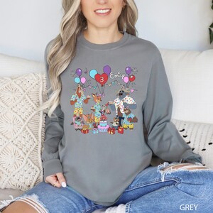 A woman wearing a gray long-sleeved shirt with a colorful graphic design featuring cartoon animals and balloons.