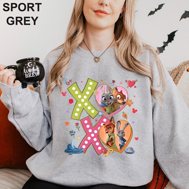 A woman wearing a grey sweatshirt with a cartoon character design on it, holding a black mug.