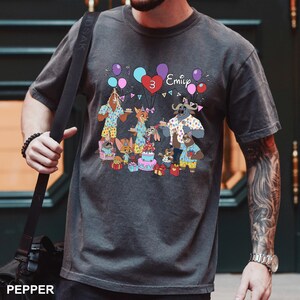 A person wearing a gray t-shirt with a birthday-themed graphic design featuring cartoon animals and a birthday cake.