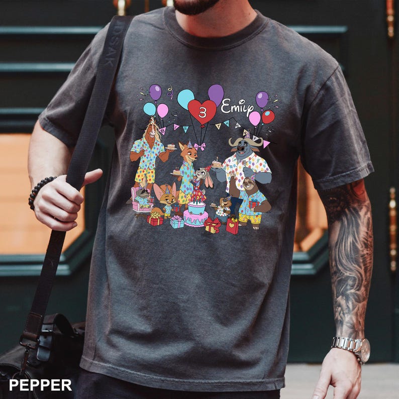 A person wearing a gray t-shirt with a birthday-themed graphic design featuring cartoon animals and a birthday cake.