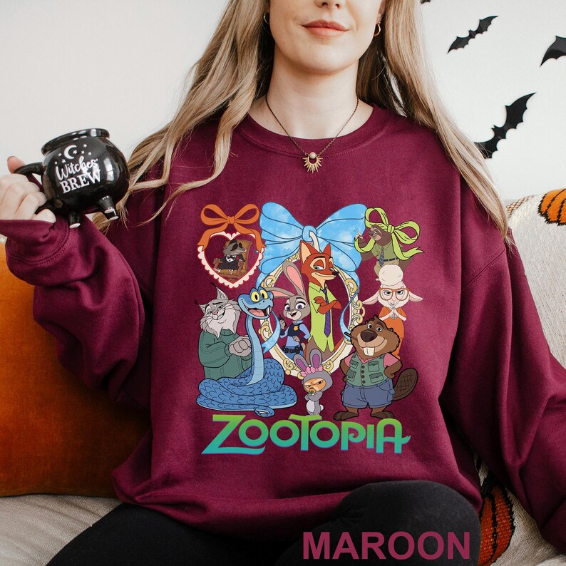 A woman wearing a burgundy sweatshirt with a cartoon character design and holding a black mug.