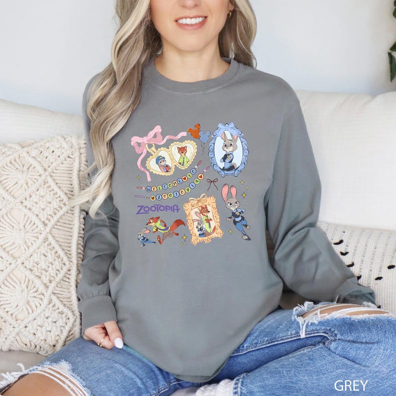 A woman wearing a grey long-sleeved shirt with a graphic design featuring cartoon characters and text.