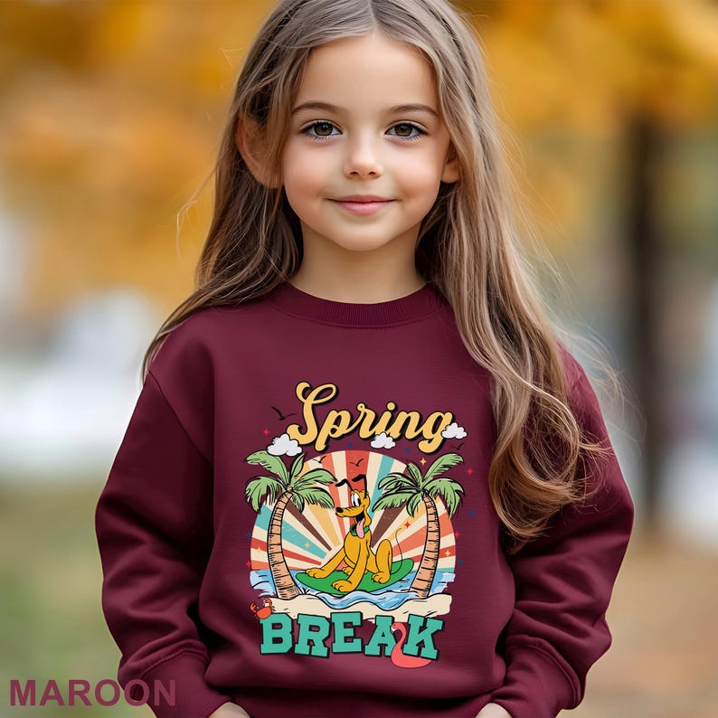 A young girl with long blonde hair wearing a maroon sweater with a cartoon character and the text "Spring Break" printed on it.