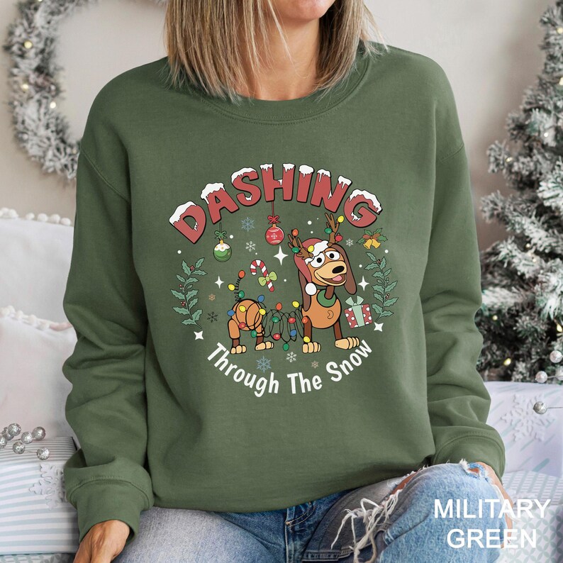 A woman wearing a green sweatshirt with a Christmas-themed design, including a cartoon dog and snowflakes.