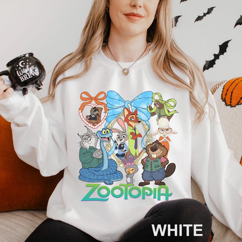 A woman wearing a white sweatshirt with a colorful cartoon character design on it, holding a mug with a black design.