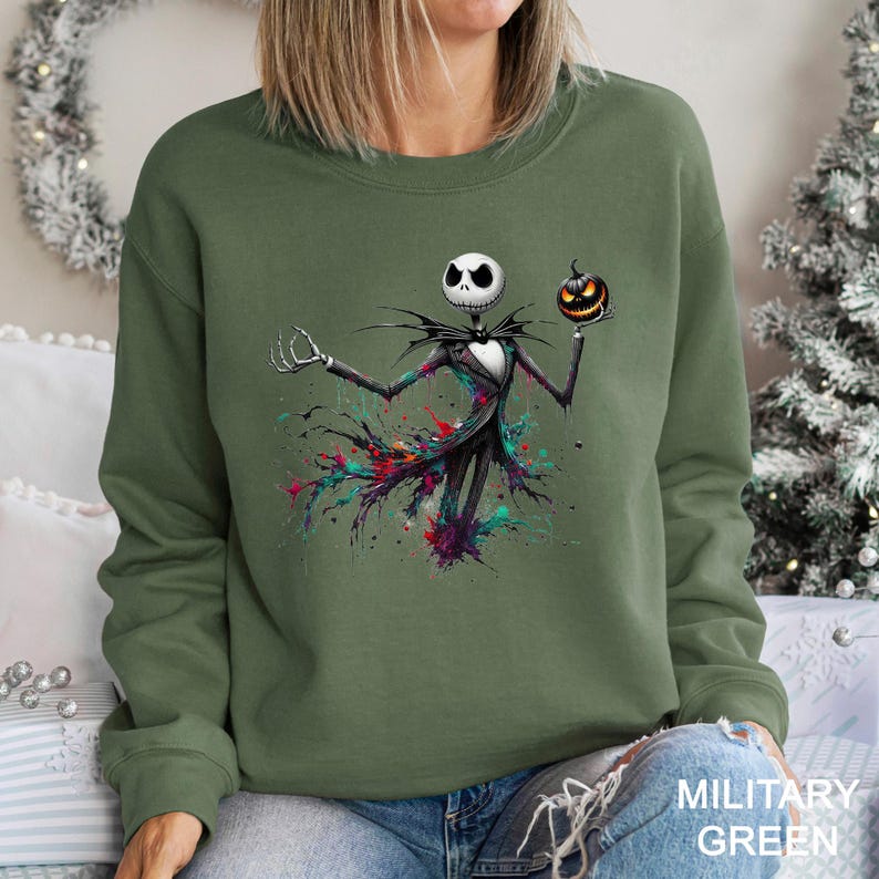 A woman wearing a green sweatshirt with a graphic of a skeleton figure holding a pumpkin and a jack-o-lantern.