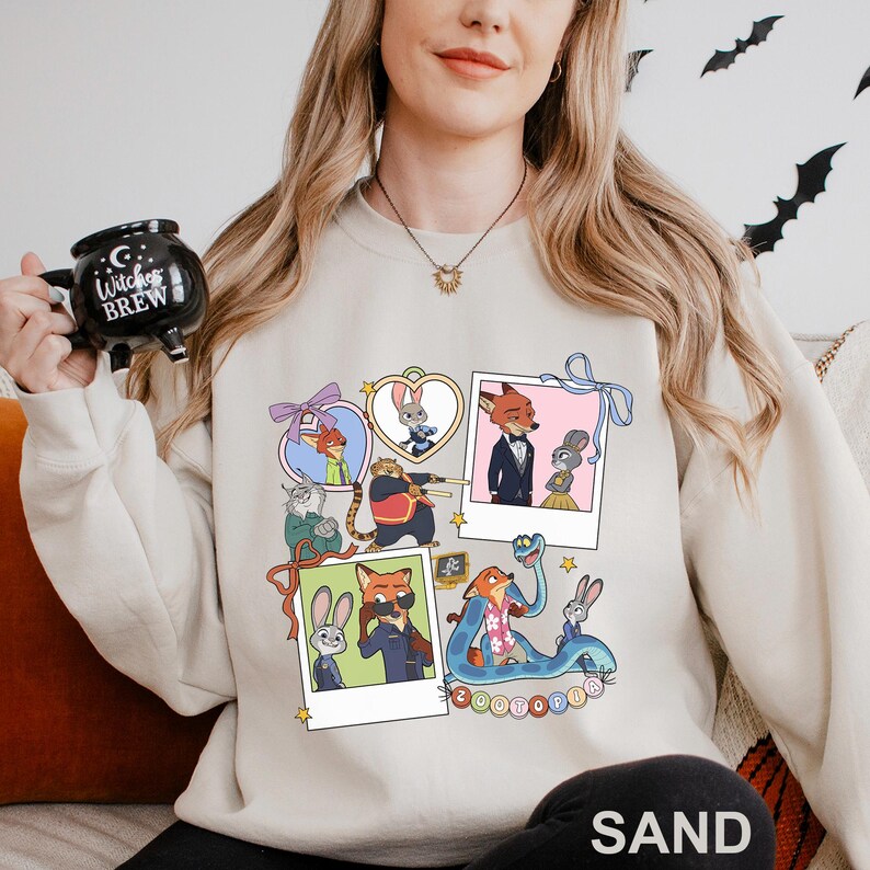 A woman wearing a white sweatshirt with a graphic of cartoon animals and a mug with the text "Witch's Brew" on it.