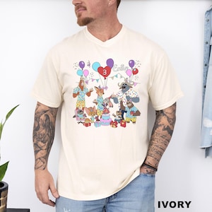 A man wearing a white t-shirt with a colorful graphic of cartoon animals and balloons, along with the text "Emilie".