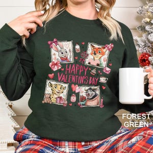 A woman wearing a green sweater with a graphic design featuring cartoon animals and the text "Happy Valentine's Day". She is holding a white mug.