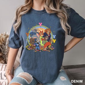 A woman wearing a blue t-shirt with a colorful graphic of various cartoon characters, including Mickey Mouse and other popular characters, on a floral background.