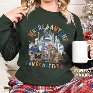 A person wearing a green sweatshirt with a colorful graphic of cartoon animals and the text "WHERE ANYONE CAN BE ANYTHING" printed on it.