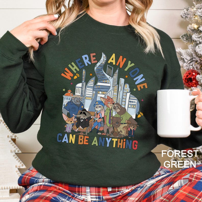A person wearing a green sweatshirt with a colorful graphic of cartoon animals and the text "WHERE ANYONE CAN BE ANYTHING" printed on it.