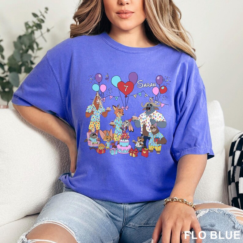 A woman wearing a blue t-shirt with a cartoon image of animals celebrating a birthday.