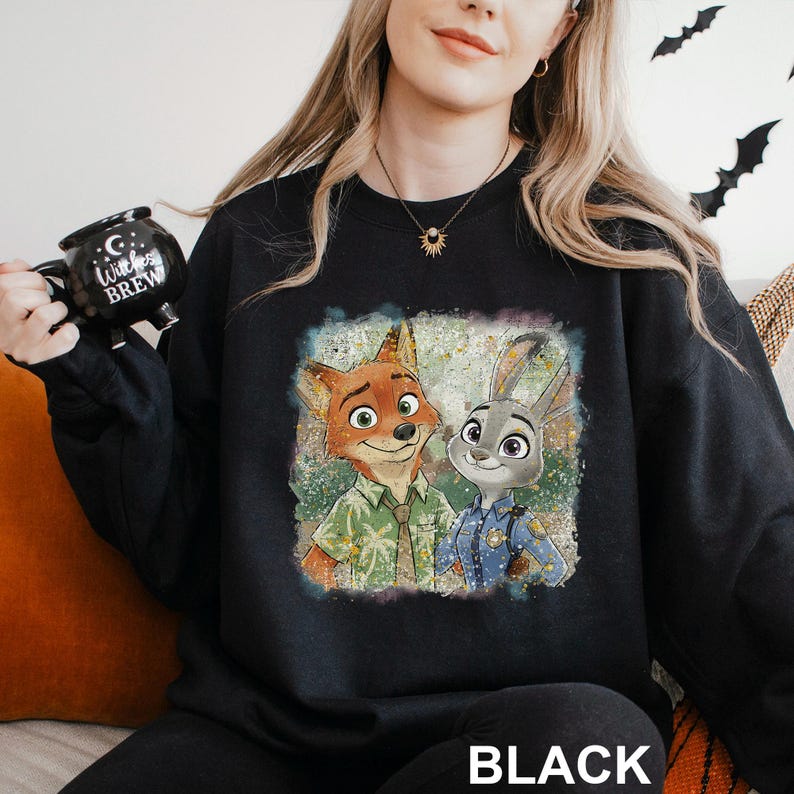 A woman wearing a black sweatshirt with a graphic of two cartoon animals, a fox and a rabbit, sitting together.