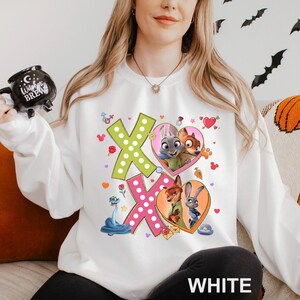 A woman wearing a white sweatshirt with a colorful graphic design featuring cartoon characters and a large "X" on the front.