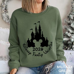 A woman wearing a green sweatshirt with a black silhouette of a castle and the text "Disney 2020 Family Vacation" printed on it.