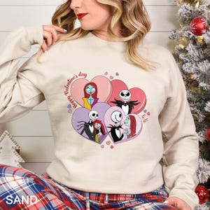 A woman wearing a white sweatshirt with a graphic of characters from the movie " Nightmare Before Christmas" and hearts around them.
