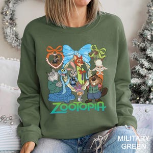 A woman wearing a green sweatshirt with a graphic of various cartoon animals, including a snake, cat, rabbit, and beaver, along with the word "Zootopia" printed on it.