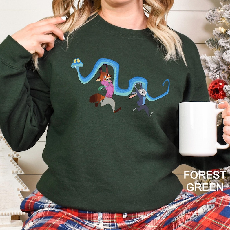 A woman wearing a green sweater with a cartoon character design is holding a white mug.