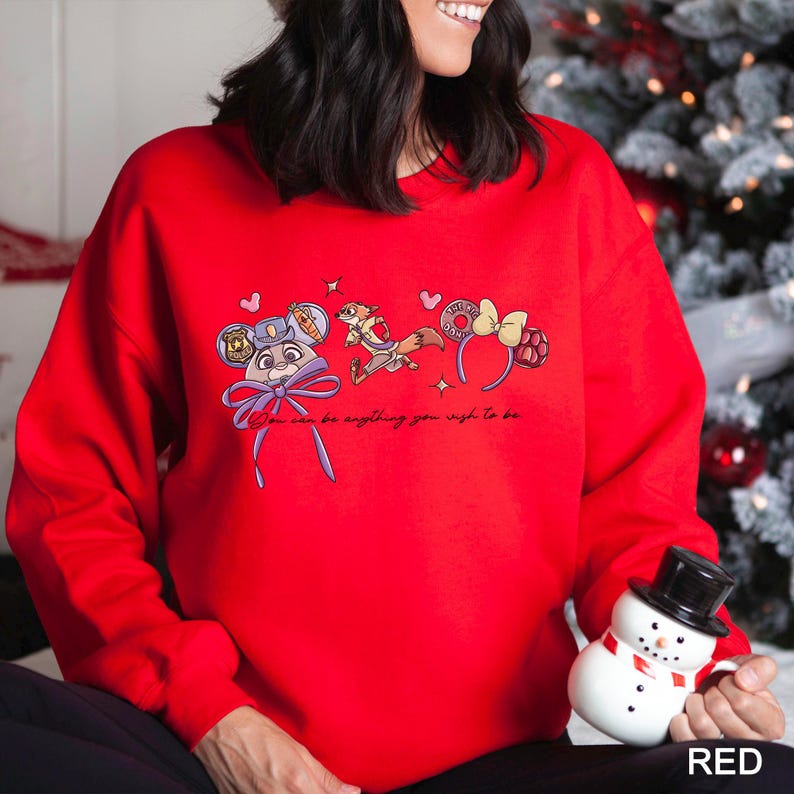 A woman wearing a red sweater with a cartoon character and text printed on it, holding a snowman and a mug.