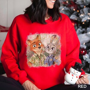 A woman wearing a red sweater with a graphic of two cartoon characters, a fox and a rabbit, smiling and posing together.