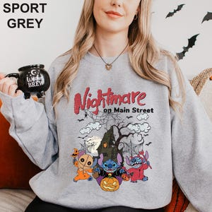 A woman wearing a grey sweatshirt with a Halloween-themed design featuring characters from the movie "Nightmare on Main Street".