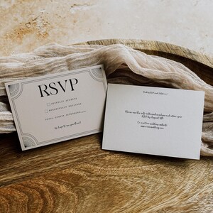 May include: Two RSVP cards with art deco design elements. The front card reads "RSVP" with checkboxes for acceptance or regret, and space for guest count. The back card has instructions for returning the RSVP. The cards are on a wooden surface.