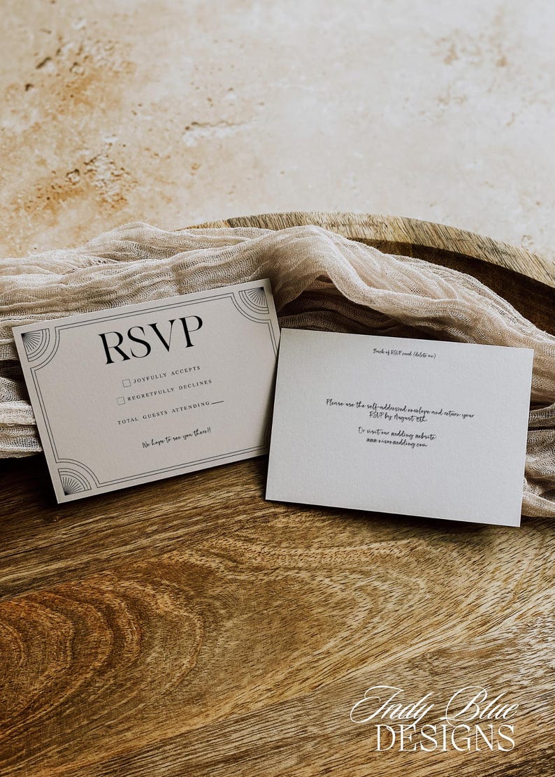 May include: Two RSVP cards with art deco design elements. The front card reads "RSVP" with checkboxes for acceptance or regret, and space for guest count. The back card has instructions for returning the RSVP. The cards are on a wooden surface.