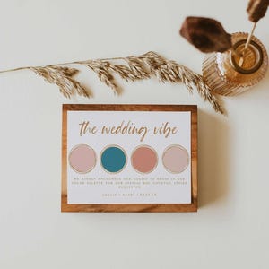 May include: A wooden framed wedding color palette card with the text "the wedding vibe". The card features four color swatches: pink, teal, coral, and light pink. The text encourages guests to dress in the color palette for the special day.