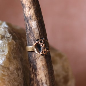 May include: A gold ring with a textured, black, circular design. The ring is on a brown, textured surface.