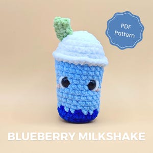 Puede incluir: Un juguete de peluche de batido de arándanos tejido a crochet con una parte superior de crema batida blanca y una pajita verde. El juguete tiene un cuerpo azul con un diseño de remolino azul y blanco y ojos negros. El juguete está sentado sobre una superficie marrón claro. Patrón PDF.