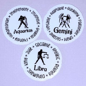 May include: Three white round stickers with black zodiac signs and personality traits. The signs are Aquarius, Gemini, and Libra. The stickers have a scalloped edge.