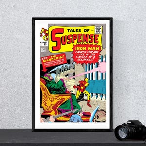 Pode incluir: Capa de banda desenhada emoldurada de "Tales of Suspense" com o Homem de Ferro. A arte da capa mostra o Homem de Ferro num fato amarelo e vermelho a lutar contra um vilão. A banda desenhada tem uma moldura preta e é exibida numa superfície escura.