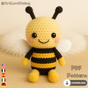 Può includere: Una bambola a forma di ape all'uncinetto con corpo giallo, strisce nere e ali bianche. L'ape ha occhi neri, guance rosa e antenne nere. L'immagine include il testo "PDF Pattern" e una freccia di download.