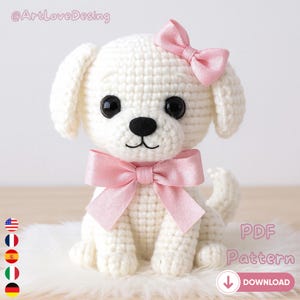 May include: A crocheted white puppy with a pink bow on its head and a pink bow around its neck. The puppy has black eyes and a black nose. The image includes the text "PDF Pattern" and a download button.